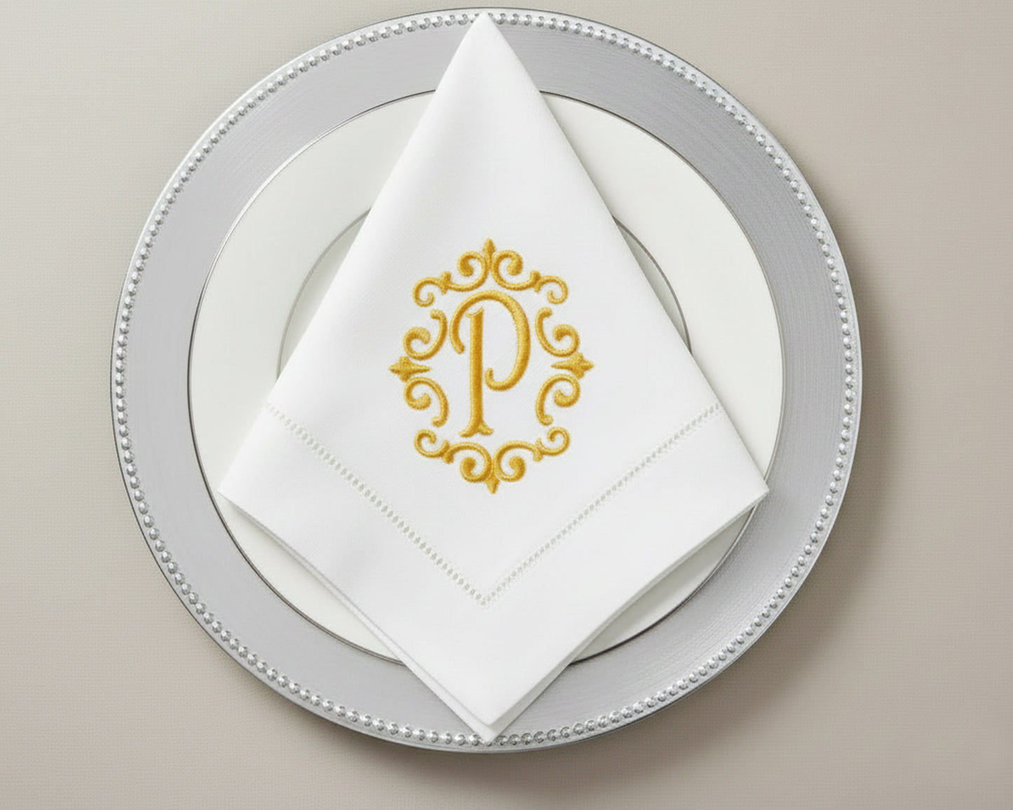 Custom embroidered cotton napkin featuring gold ornate P monogram, styled in triangle fold on formal table setting