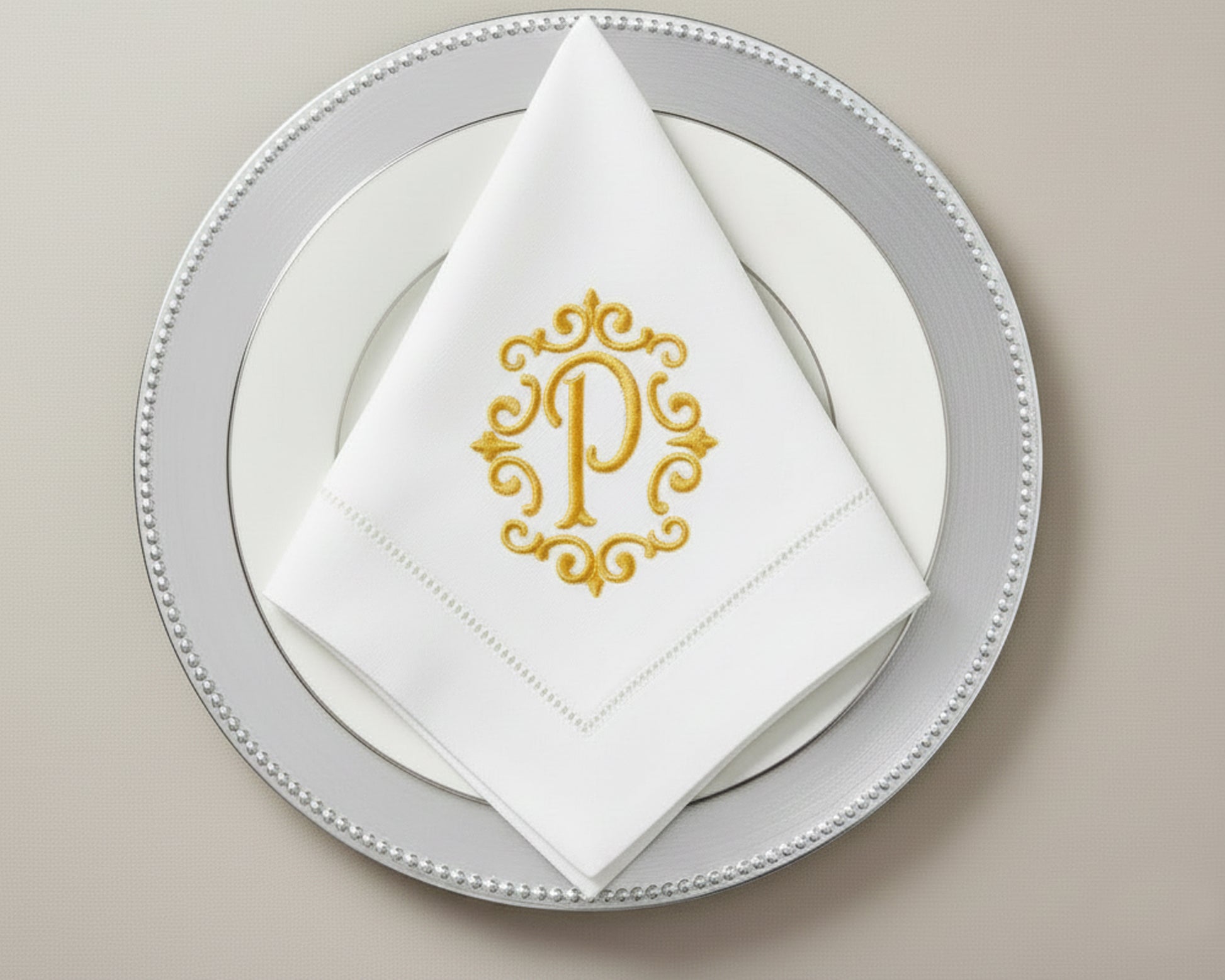 Custom embroidered cotton napkin featuring gold ornate P monogram, styled in triangle fold on formal table setting