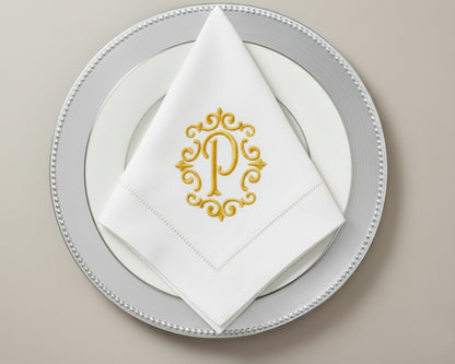 Custom embroidered cotton napkin featuring gold ornate P monogram, styled in triangle fold on formal table setting