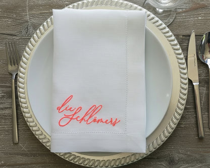 A personalized white linen napkin with coral embroidery placed on a silver-rimmed charger plate with formal cutlery