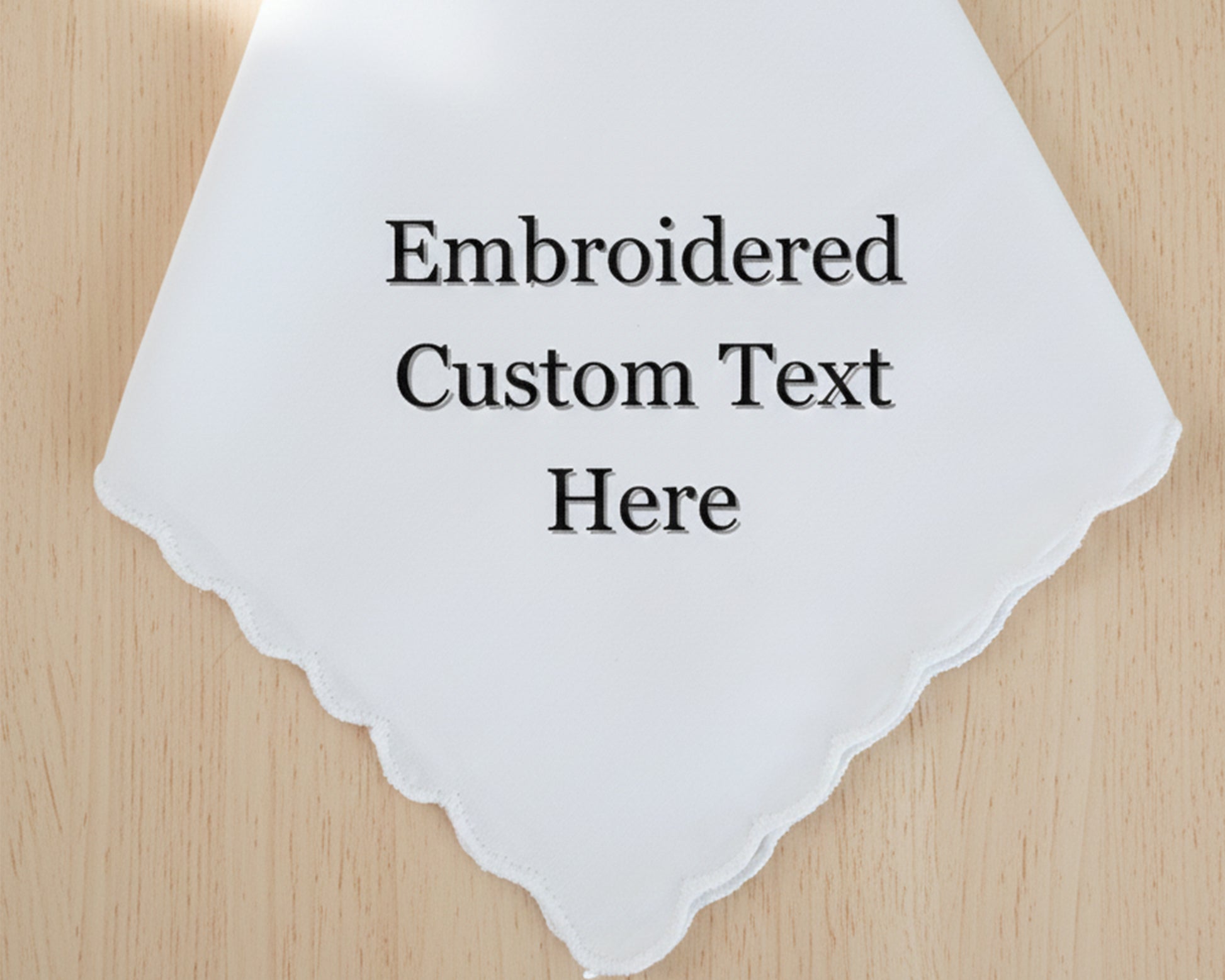 A white cotton handkerchief with a delicate scalloped edge, showcasing a placeholder for custom embroidered text in a classic serif font.