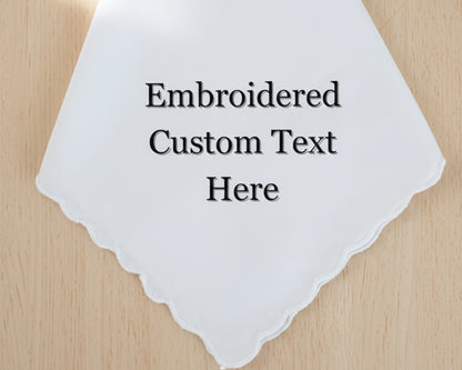 A white cotton handkerchief with a delicate scalloped edge, showcasing a placeholder for custom embroidered text in a classic serif font.