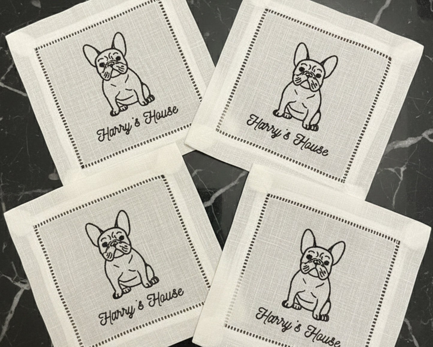 A close-up of a premium white cotton beverage coaster with a hemstitch border, personalized with a detailed machine-embroidered dog illustration and cocktail icon.