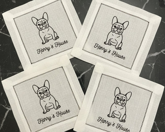 A close-up of a premium white cotton beverage coaster with a hemstitch border, personalized with a detailed machine-embroidered dog illustration and cocktail icon.