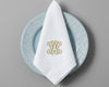 Custom monogrammed white linen napkin with gold embroidered initial displayed on blue decorative plate