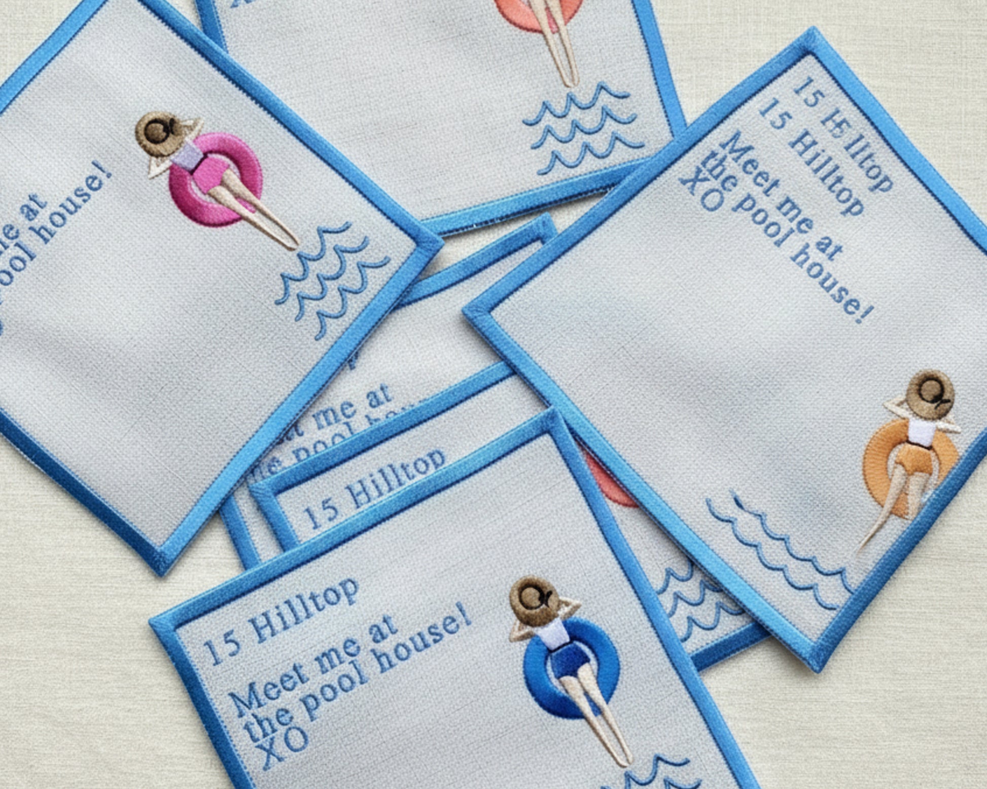 A stack of white linen cocktail napkins with blue borders, featuring custom address embroidery and a girl in a pink floaty.