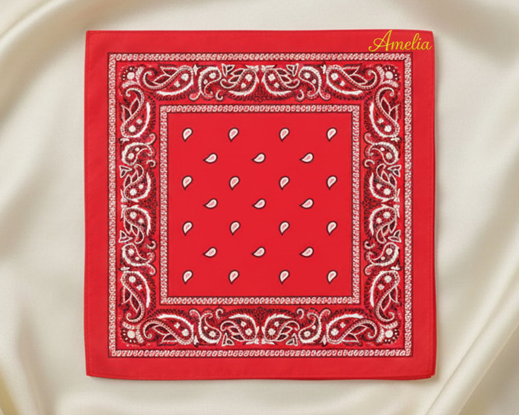 A flat lay of a classic red paisley bandana featuring the name "Amelia" in elegant yellow chain stitch embroidery.