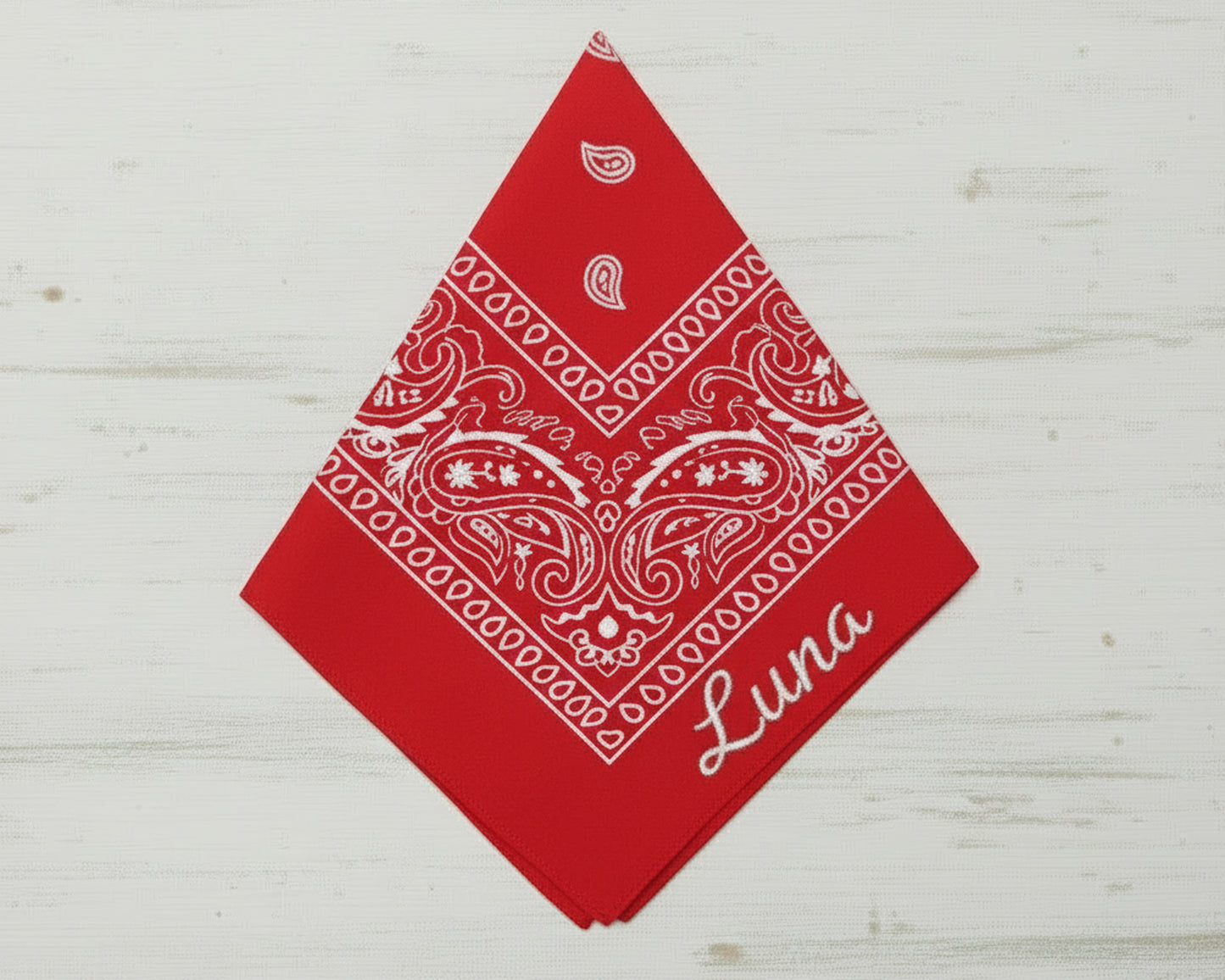 A vibrant red paisley pet bandana personalized with the name "Luna" in a white textured script.