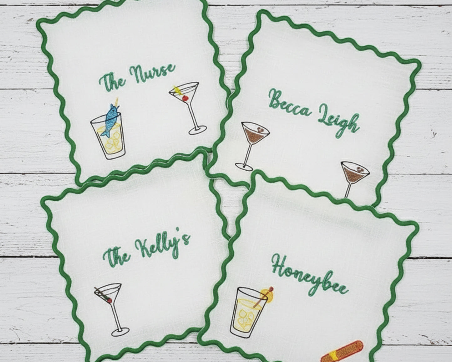 A collection of various colored scalloped fabric coasters, including sky blue, peach, and cream, featuring personalized embroidery for "Daniella's Cocktail Bar".