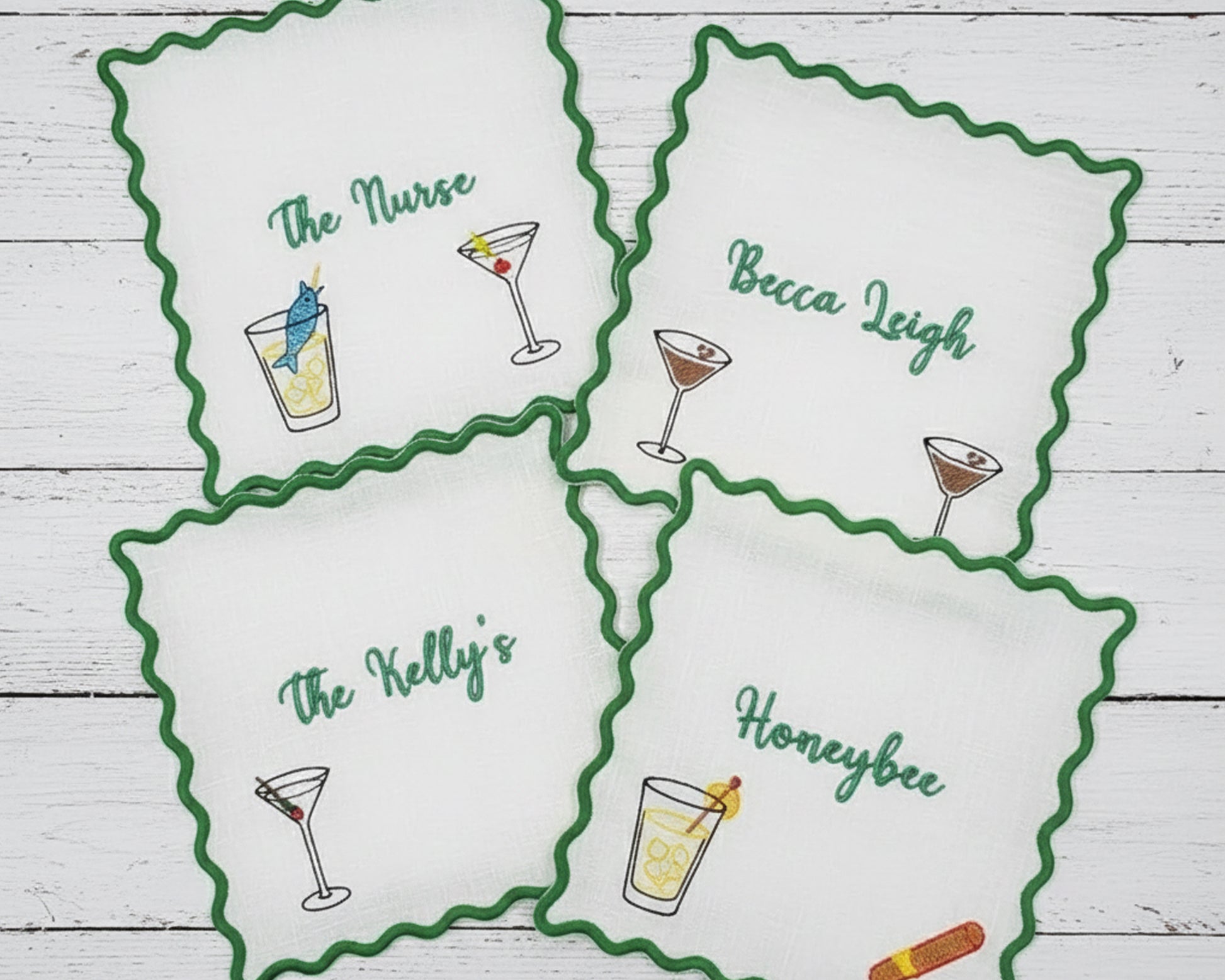 A collection of various colored scalloped fabric coasters, including sky blue, peach, and cream, featuring personalized embroidery for "Daniella's Cocktail Bar".