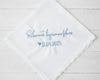 Personalized Spanish wedding handkerchief with a heart and the phrase "Solamente lágrimas felices" in light blue embroidery, shown on soft pink silk.