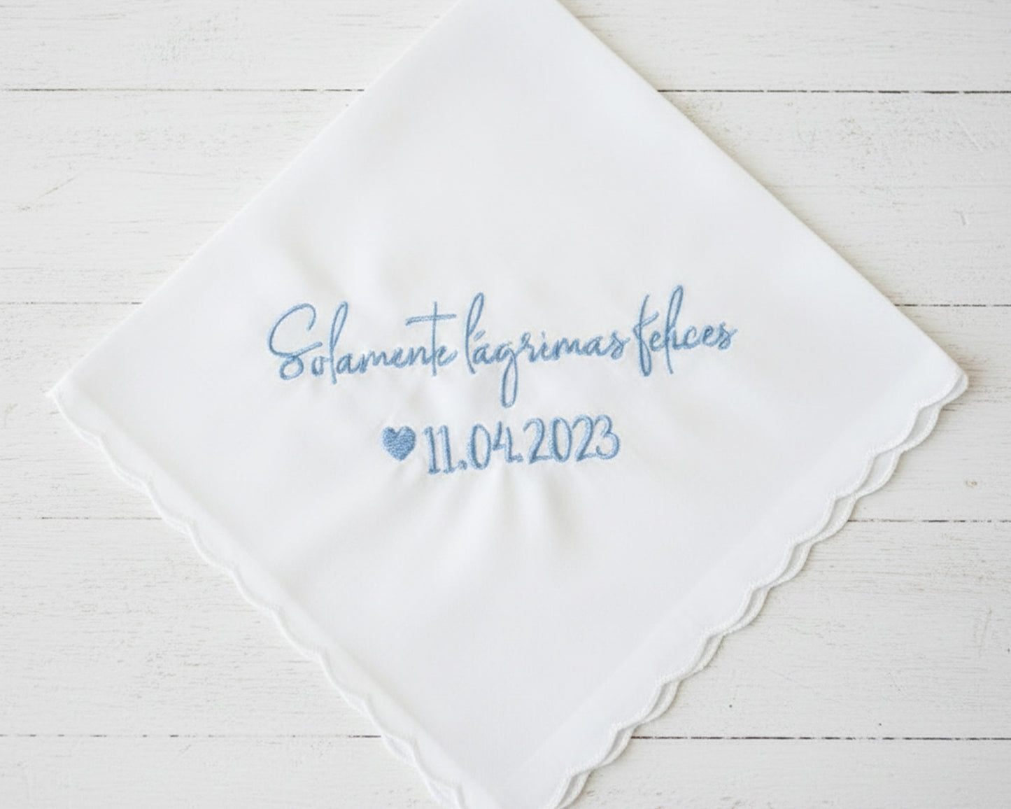 Personalized Spanish wedding handkerchief with a heart and the phrase "Solamente lágrimas felices" in light blue embroidery, shown on soft pink silk.