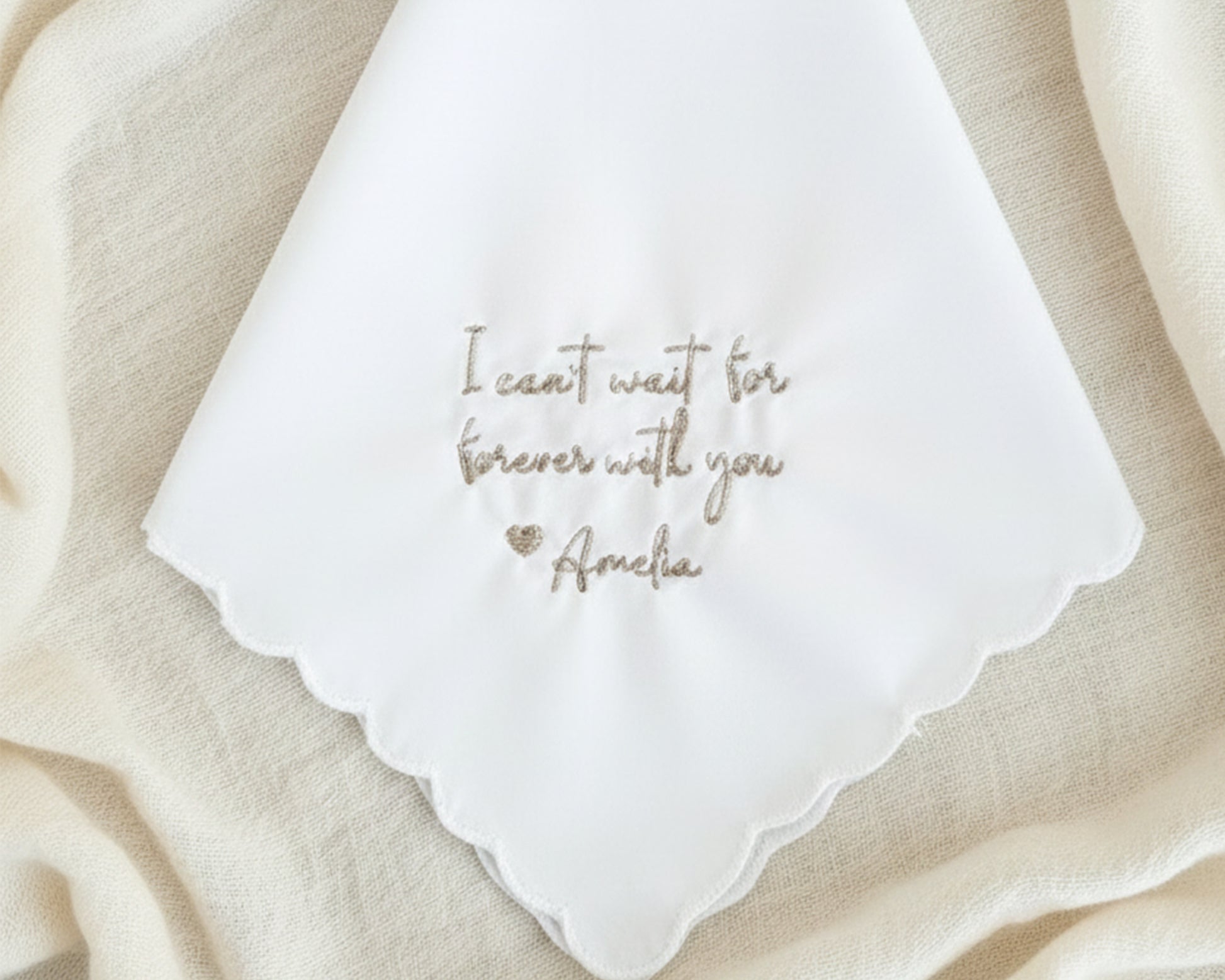 A white scalloped cotton handkerchief embroidered with "I can't wait for forever with you Amelia" in champagne gold.