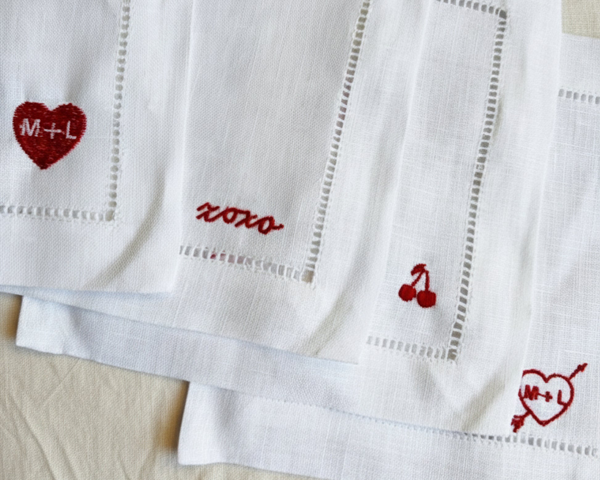 White linen napkins with red embroidered designs on a beige surface