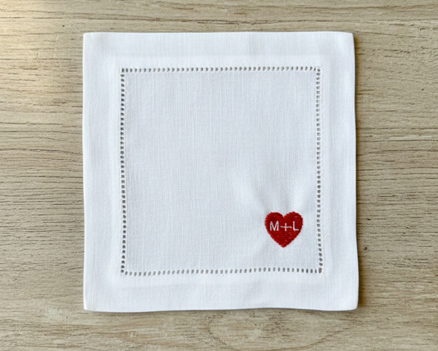 White napkin with a red heart and initials 'M+L' on a wooden surface