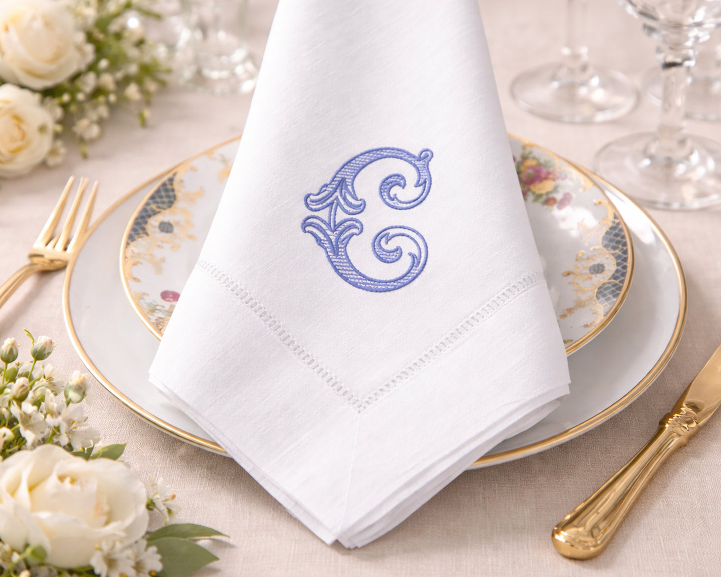 White napkin with a blue monogram on a table setting with flowers and cutlery.
