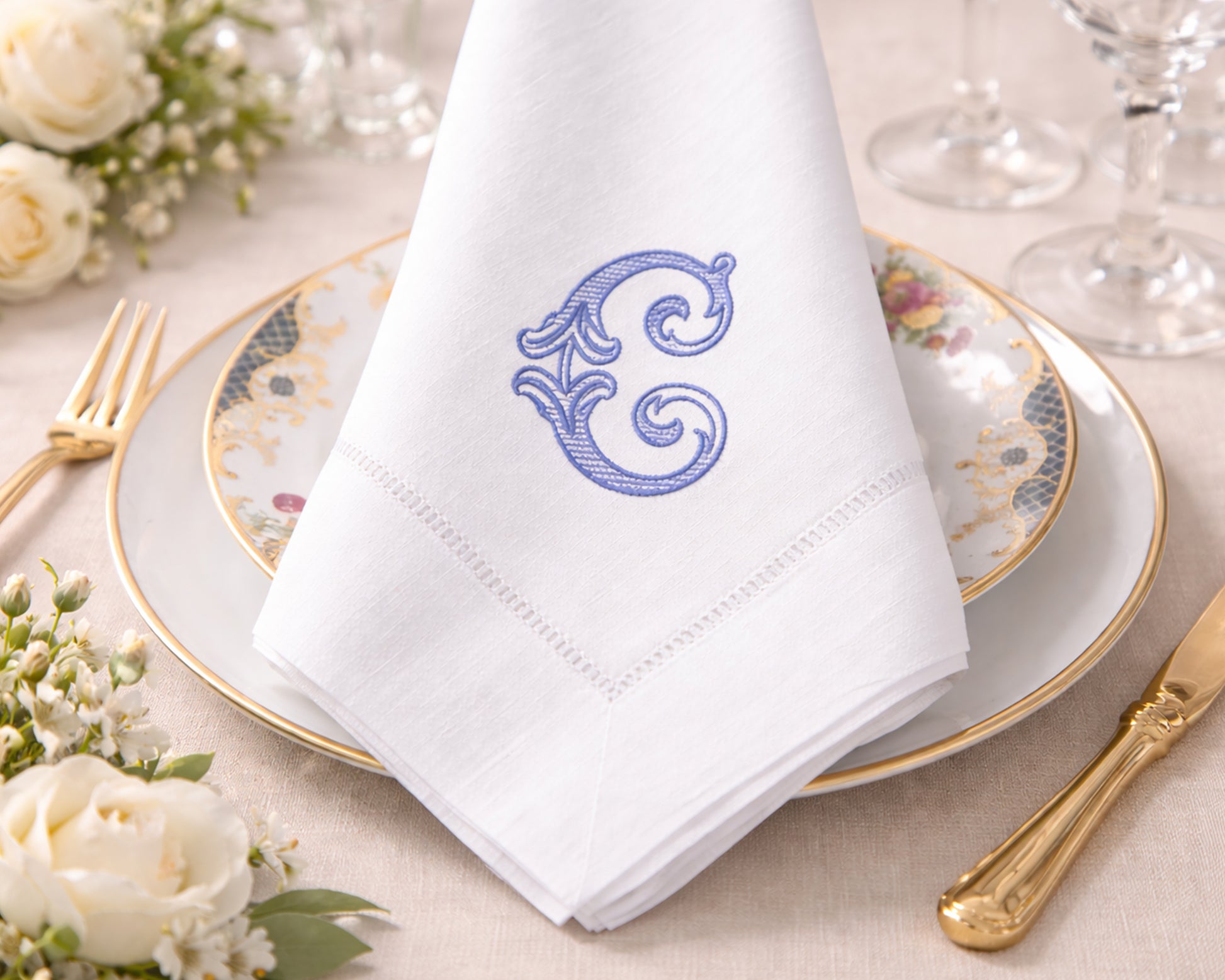 White napkin with a blue monogram on a table setting with flowers and cutlery.