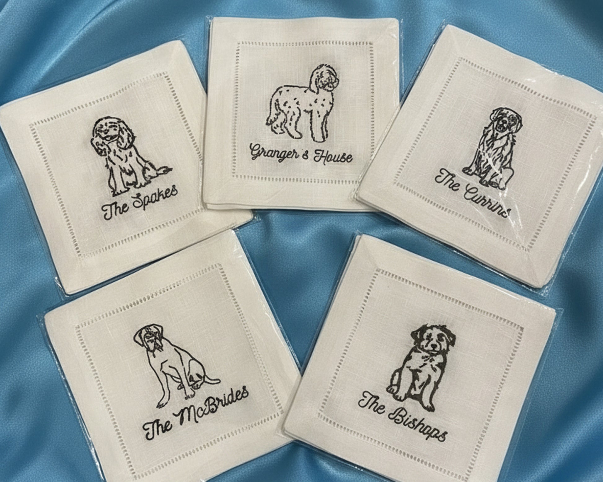 A crisp white cotton hemstitch napkin featuring a detailed black embroidered Doodle dog sitting next to a martini glass icon.