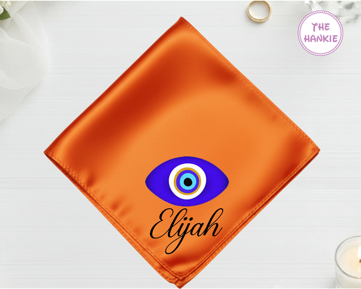 A deep sunset orange high-lustre satin pocket square customized with "Elijah" and a vibrant geometric blue and white protective eye icon.