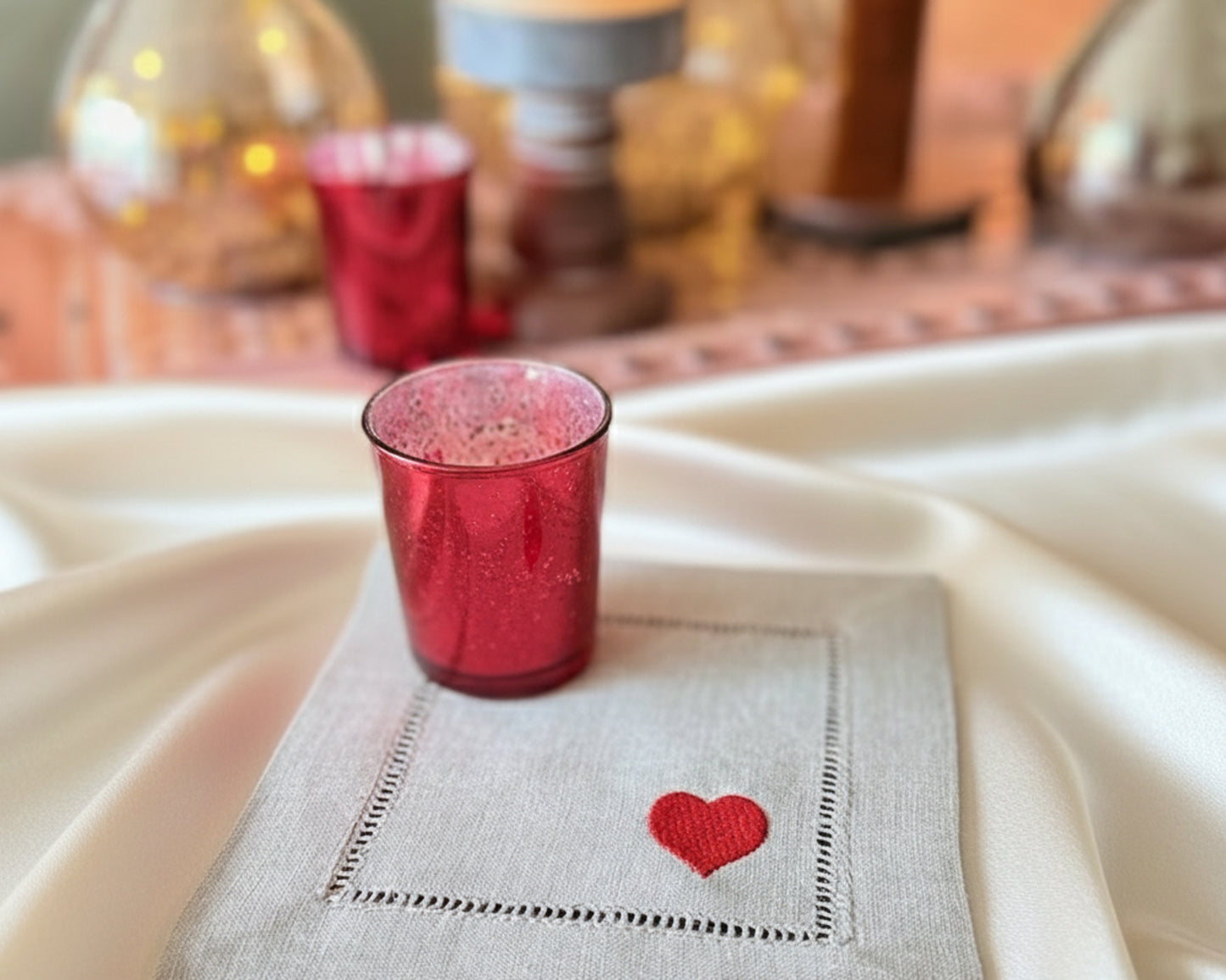 Red glass candle holder on a white napkin with a red heart design, placed on a textured surface.