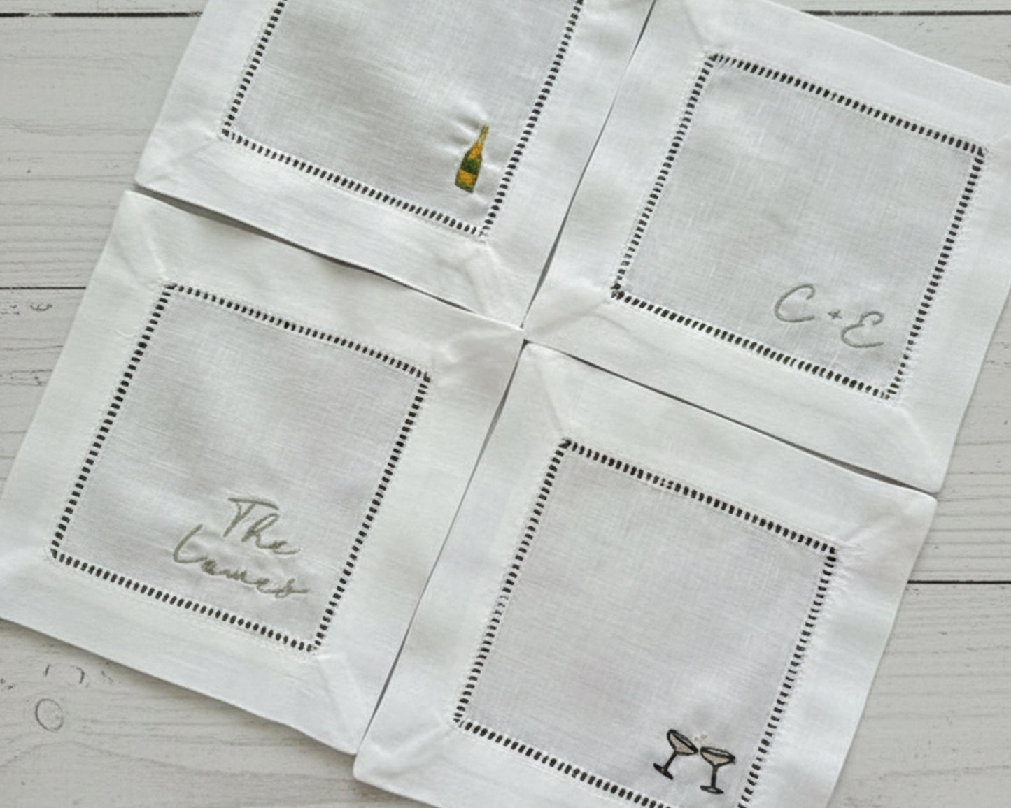Close-up of custom embroidered linen bar coasters with hemstitch borders on a light wood surface.
