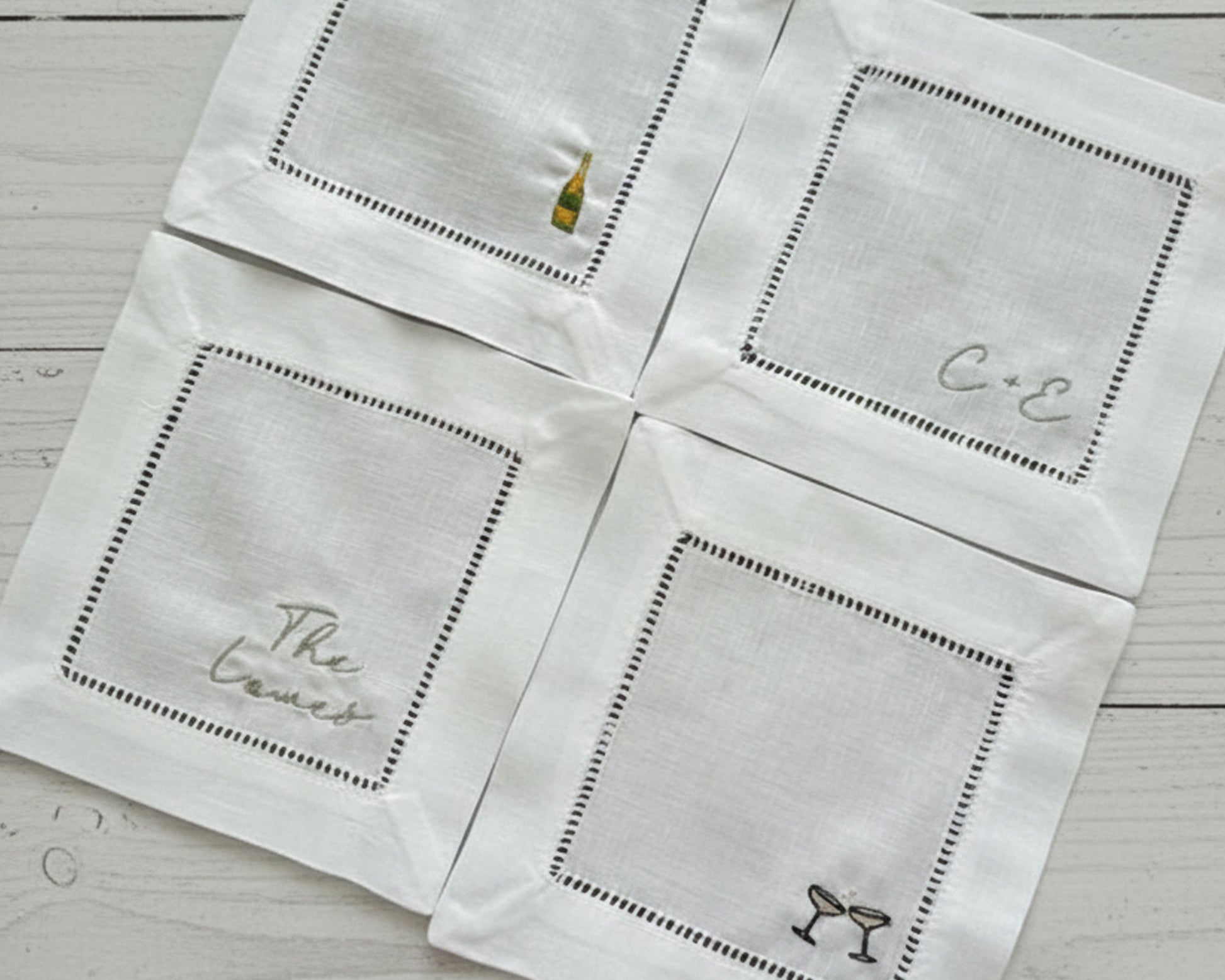 Close-up of custom embroidered linen bar coasters with hemstitch borders on a light wood surface.