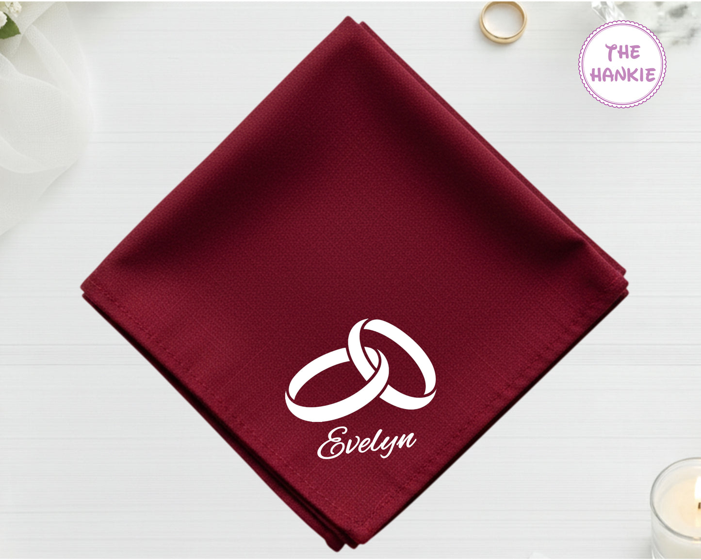 A deep burgundy cotton handkerchief customized with the name "Evelyn" and a white embroidered design of two interlocking wedding bands.