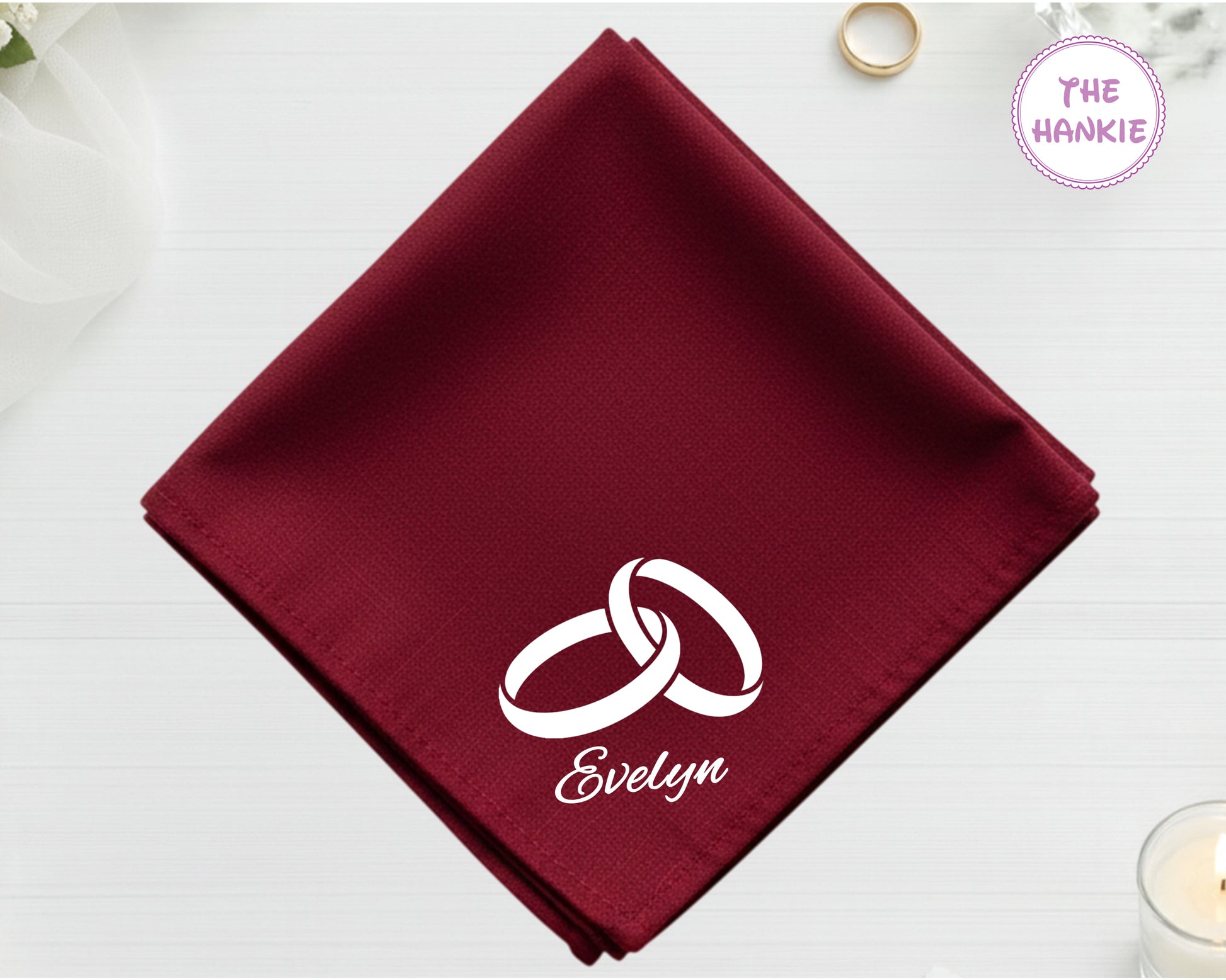 A deep burgundy cotton handkerchief customized with the name "Evelyn" and a white embroidered design of two interlocking wedding bands.
