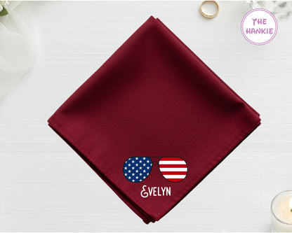 A spring maroon cotton handkerchief customized with the name "evelyn" and a vibrant, waving American flag embroidery.