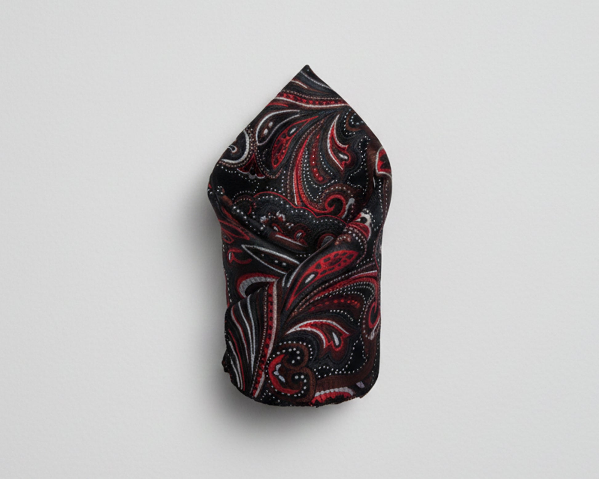 Close up of a crimson paisley silk pocket square styled in a classic puff fold showing the intricate silk texture.
