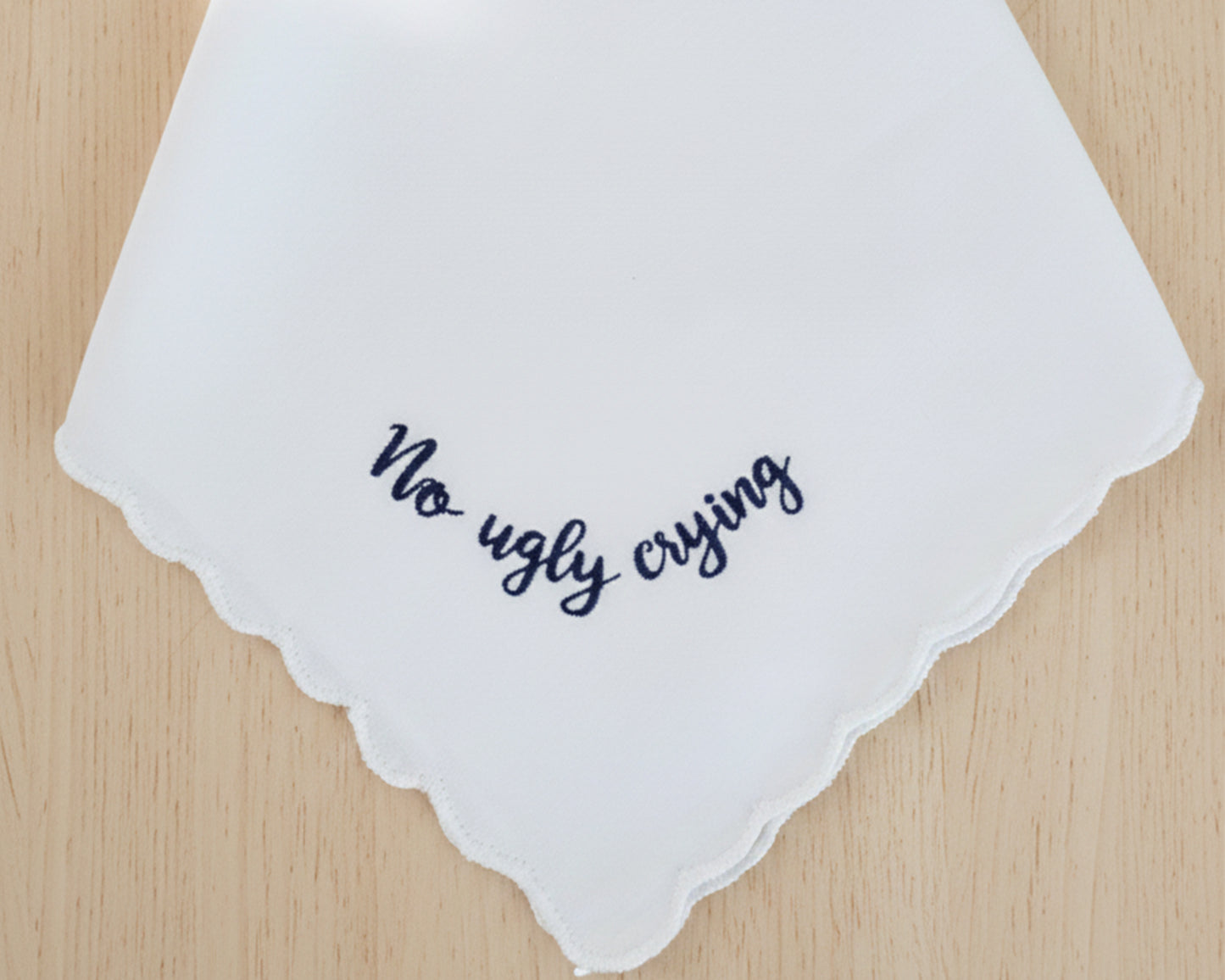 A personalized white wedding handkerchief with a scalloped border, featuring a humorous navy blue embroidered message that says "No ugly crying".