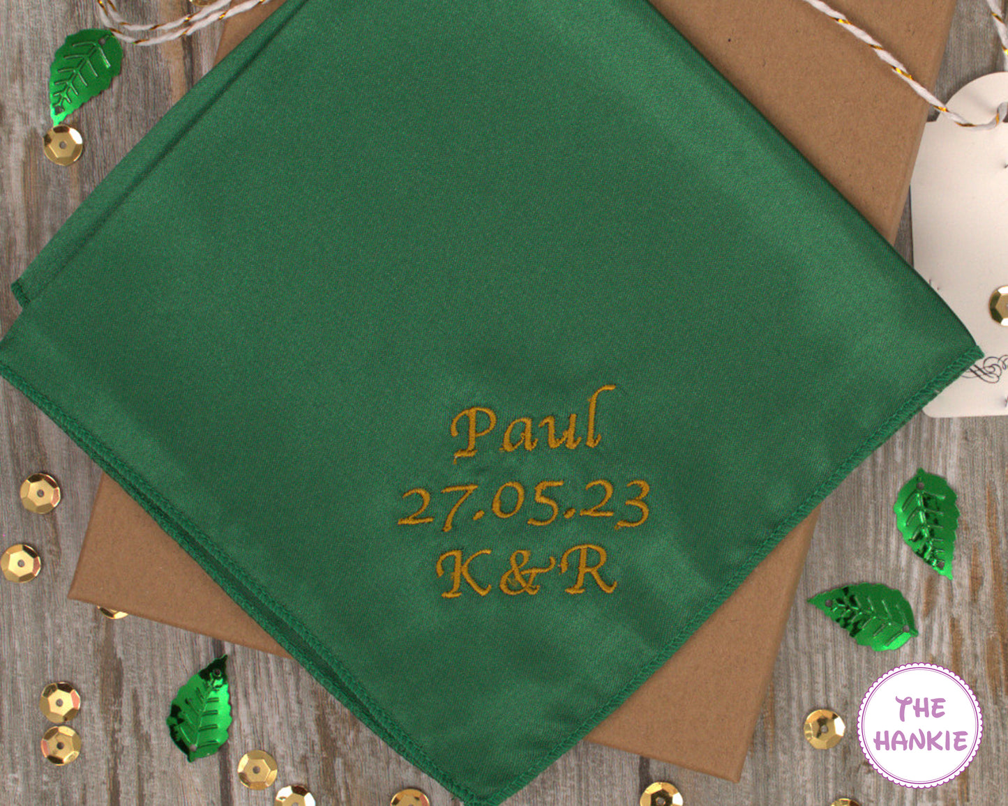 Green handkerchief with embroidered text on a wooden surface with decorative elements.