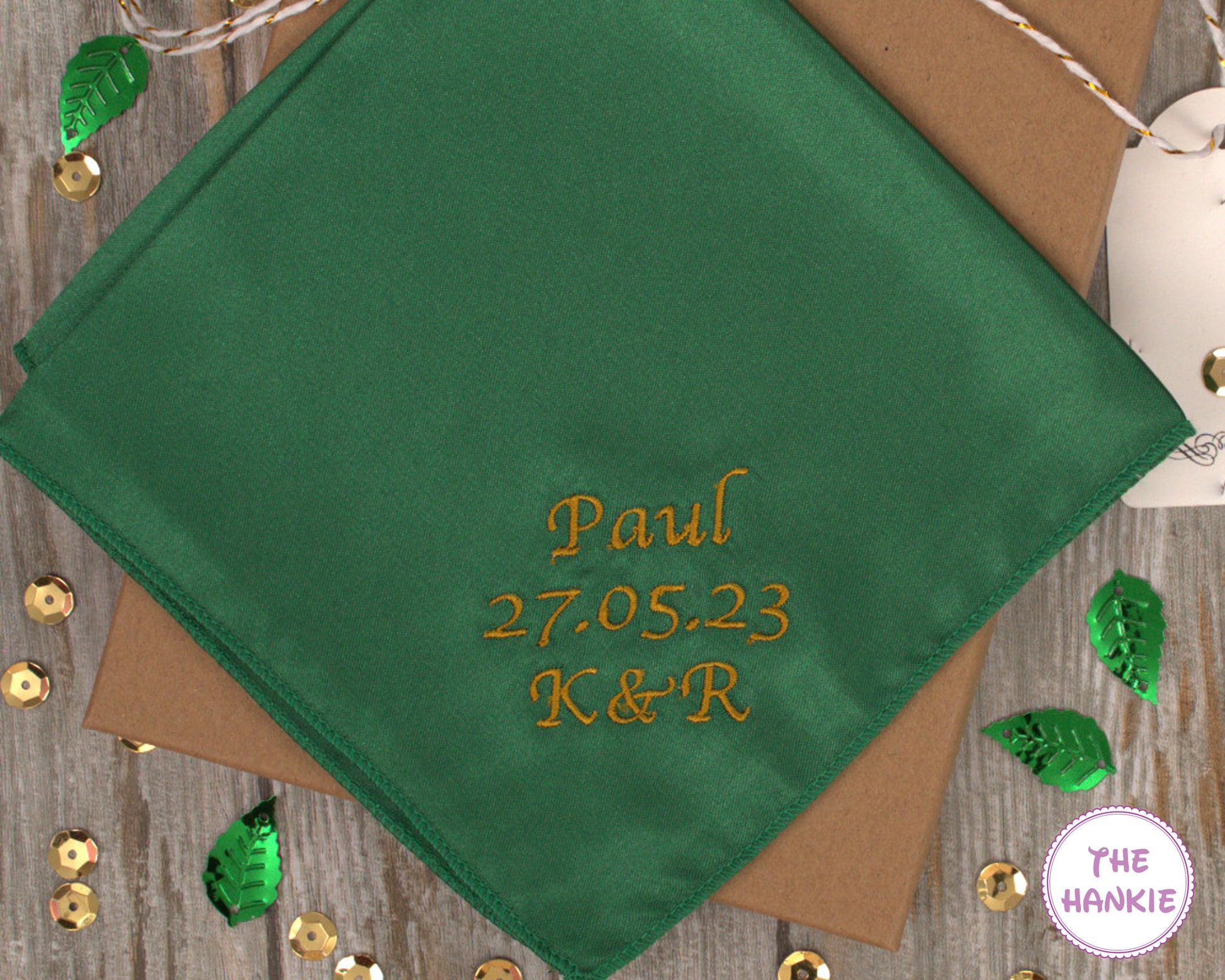 Green handkerchief with embroidered text on a wooden surface with decorative elements.
