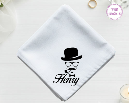A crisp white cotton handkerchief personalized with "Henry" below a black vinyl print of a vintage bowler hat, glasses, and a pipe.
