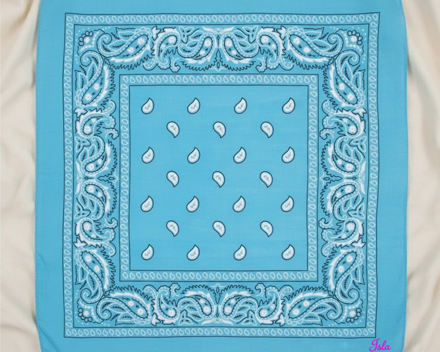 A top-down view of a bright sky blue paisley bandana with the name "Isla" custom embroidered in pink chain stitching.
