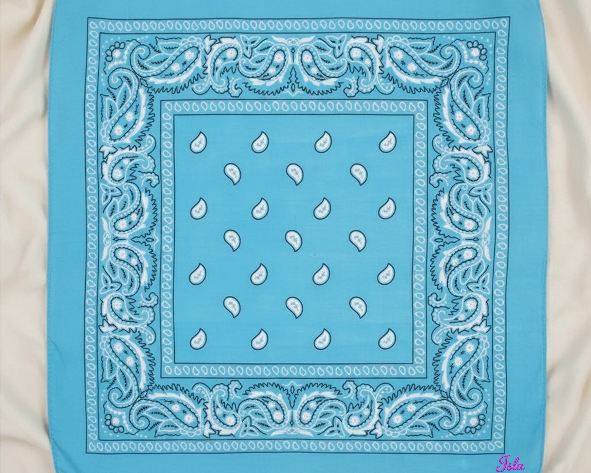 A top-down view of a bright sky blue paisley bandana with the name "Isla" custom embroidered in pink chain stitching.