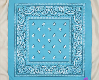 A top-down view of a bright sky blue paisley bandana with the name "Isla" custom embroidered in pink chain stitching.