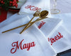 White napkins with red embroidered names on a table setting with gold cutlery.