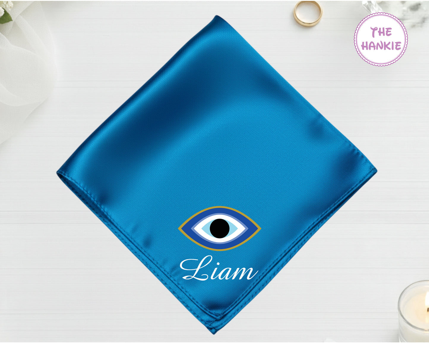 A brilliant sapphire blue luxury satin handkerchief featuring "Liam" below a minimalist blue-and-black protective eye with a gold-toned rim.