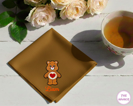 A warm caramel brown cotton handkerchief featuring the name "Liam" and a classic orange-brown Tenderheart Bear character with a heart badge.