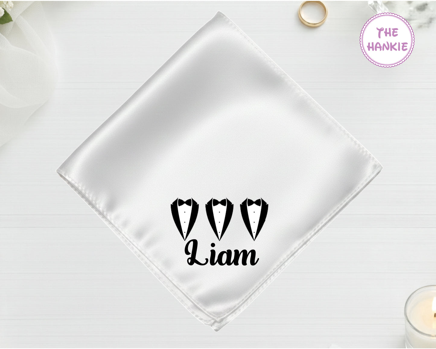 A shimmering pearl white luxury satin handkerchief personalized with "Liam" below a black vinyl print of three tuxedo lapel silhouettes.