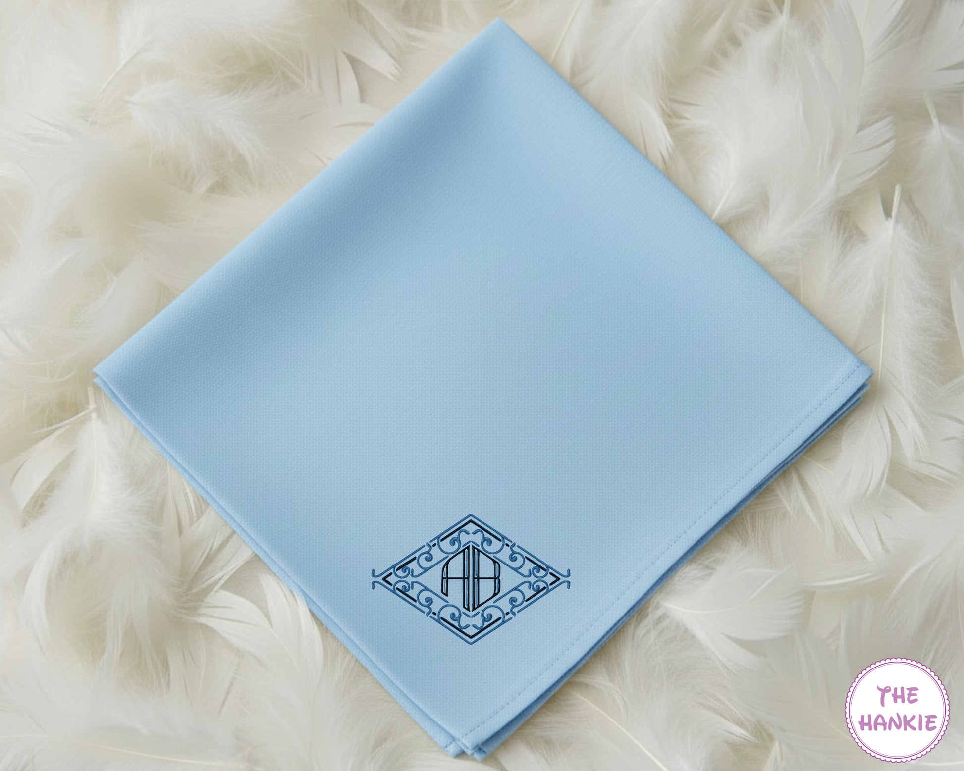 A light blue premium cotton handkerchief featuring a custom dark blue diamond crest monogram with the initials "AB".