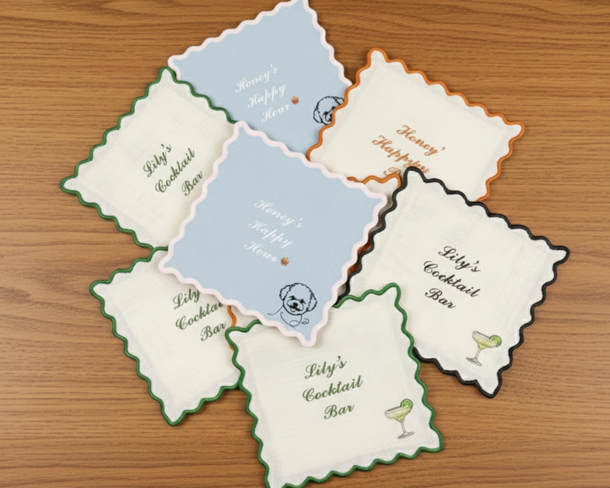 A stack of beige linen cocktail napkins with forest green scalloped edges, personalized with "Lily's Cocktail Bar" and a martini icon.