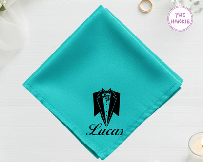 A radiant turquoise cotton handkerchief personalized with "Lucas" below a black vinyl print of a formal tuxedo silhouette with a leaf lapel detail.