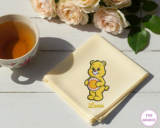 A buttery yellow cotton handkerchief personalized with the name "Lucas" and an embroidered yellow Funshine Bear character.