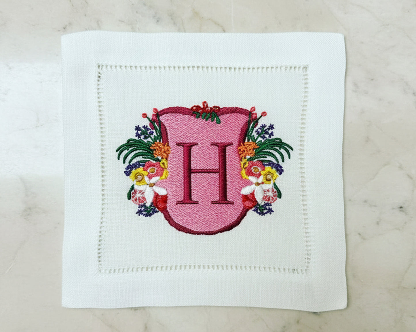 White cotton napkin with an intricate green shield crest featuring mountains and a 'R' monogram