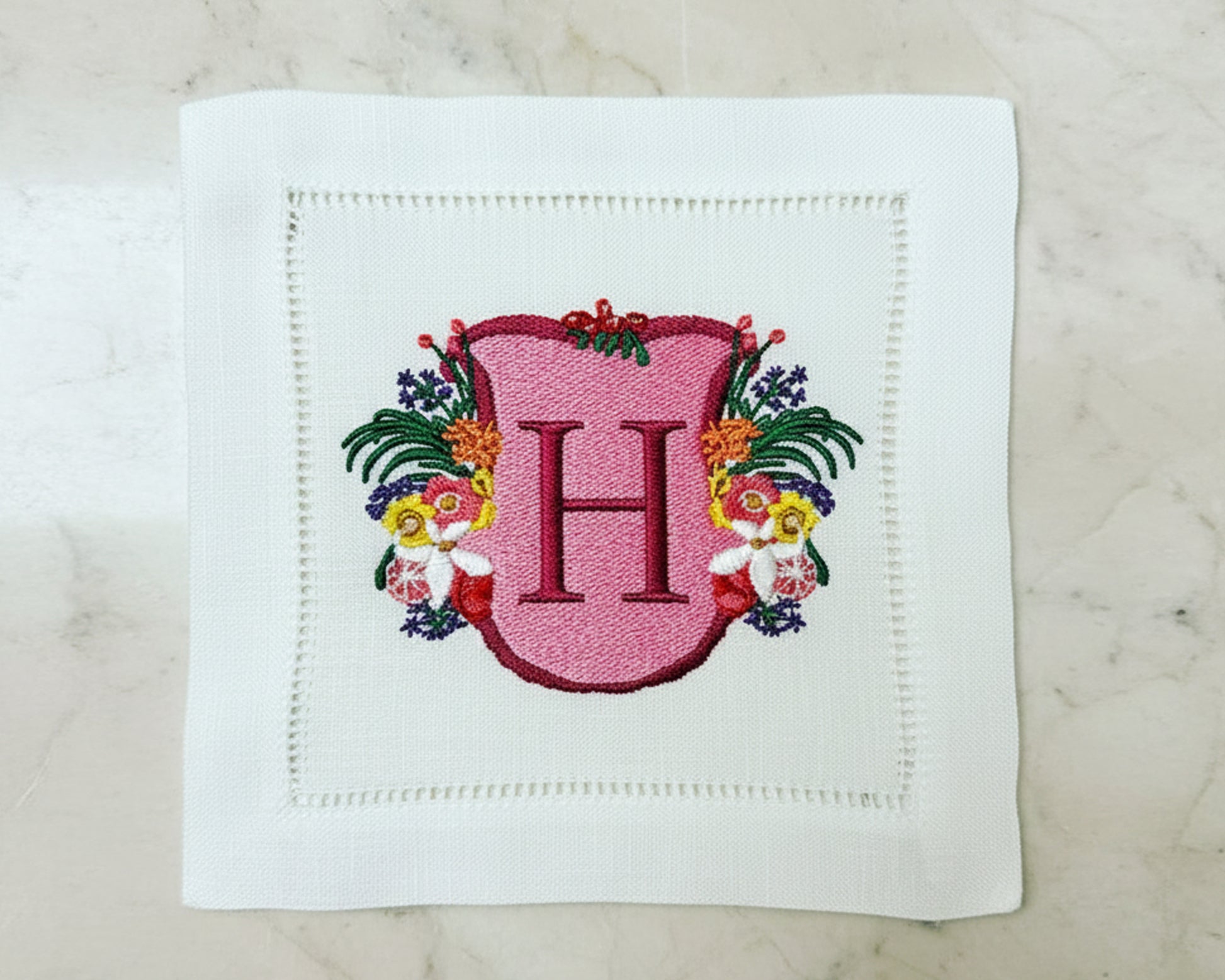 White cotton napkin with an intricate green shield crest featuring mountains and a 'R' monogram