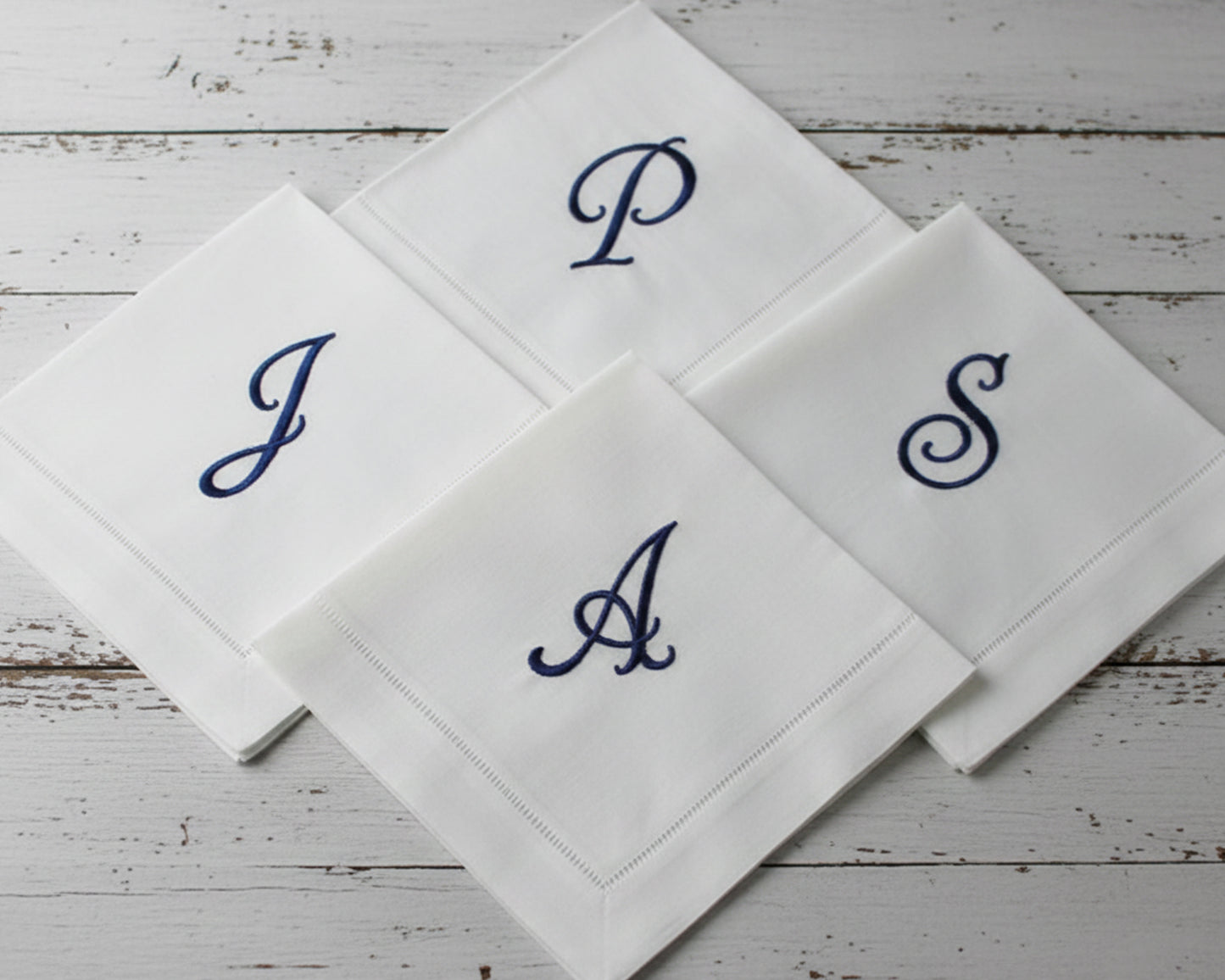 Custom embroidered white hemstitch napkin featuring a detailed green heraldic shield crest with a lion, mountain motif, and 'R' monogram