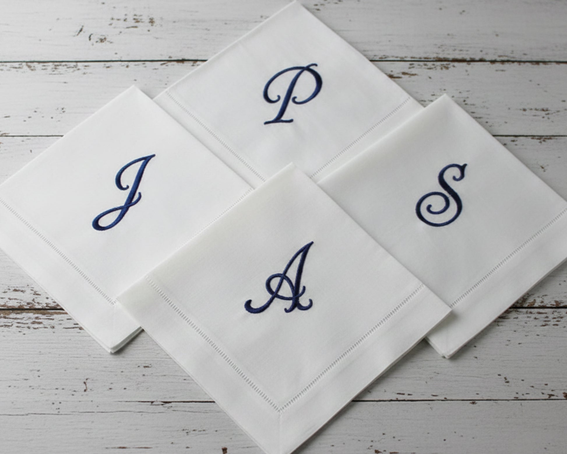 Custom embroidered white hemstitch napkin featuring a detailed green heraldic shield crest with a lion, mountain motif, and 'R' monogram