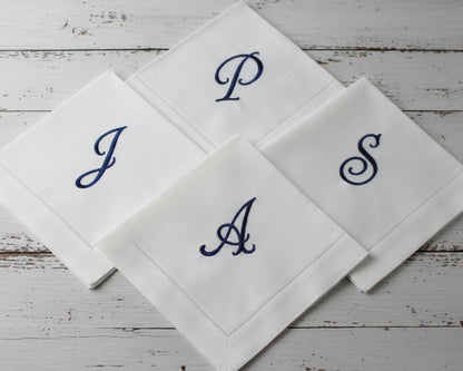 Custom embroidered white hemstitch napkin featuring a detailed green heraldic shield crest with a lion, mountain motif, and 'R' monogram
